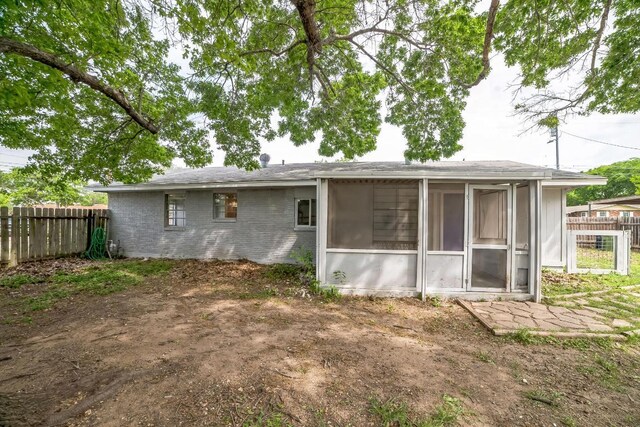 back of property with brick siding, a sunroom, and fence