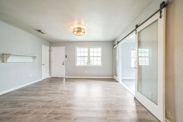 interior space with a barn door, wood finished floors, visible vents, and baseboards