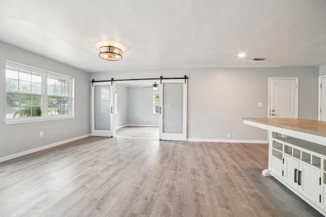 unfurnished living room featuring a barn door, baseboards, visible vents, and light wood-type flooring