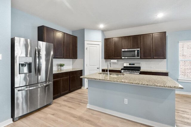 17109 Calipatria Ln, Pflugerville, TX 78660 - kitchen featuring appliances with stainless steel finishes, dark brown cabinets, light wood-type flooring, light stone countertops, and recessed lighting