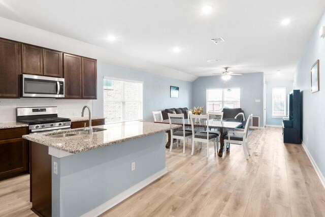 17109 Calipatria Ln, Pflugerville, TX 78660 - kitchen with appliances with stainless steel finishes, ceiling fan, a kitchen island with sink, dark brown cabinets, and light stone counters