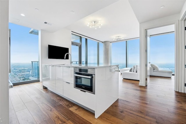 kitchen featuring open floor plan, stainless steel oven, modern cabinets, a wall of windows, and white cabinets