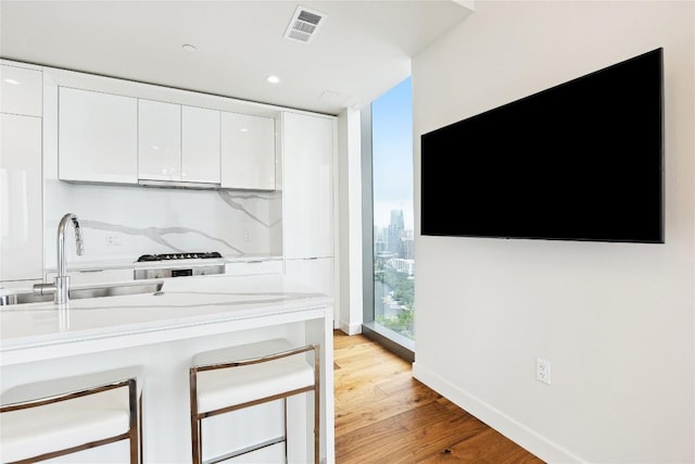 kitchen with white cabinets, light countertops, visible vents, a sink, and light wood-type flooring