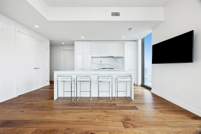 kitchen featuring visible vents, white cabinetry, modern cabinets, a breakfast bar, and an island with sink