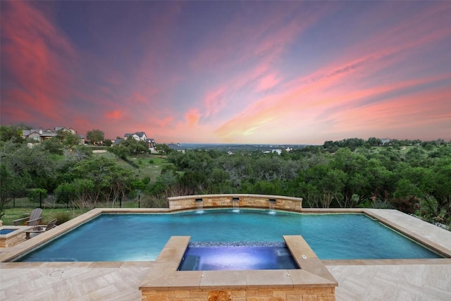 pool at dusk with a pool with connected hot tub