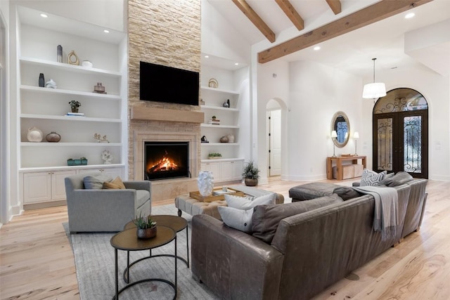 living area featuring arched walkways, light wood-style floors, baseboards, built in features, and high vaulted ceiling