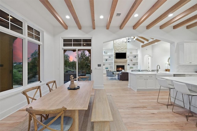 dining room featuring an inviting chandelier, visible vents, beamed ceiling, light wood-style floors, and a fireplace