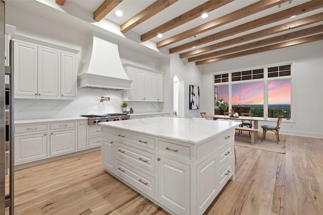 kitchen with stainless steel gas stovetop, beam ceiling, arched walkways, and custom range hood