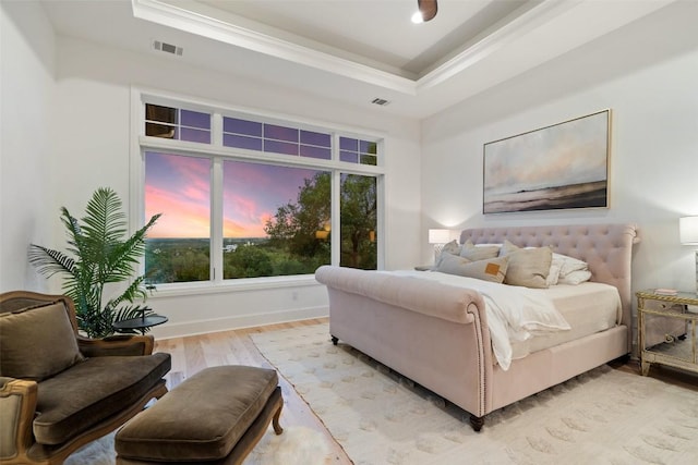 bedroom featuring light wood-type flooring, visible vents, a raised ceiling, and crown molding