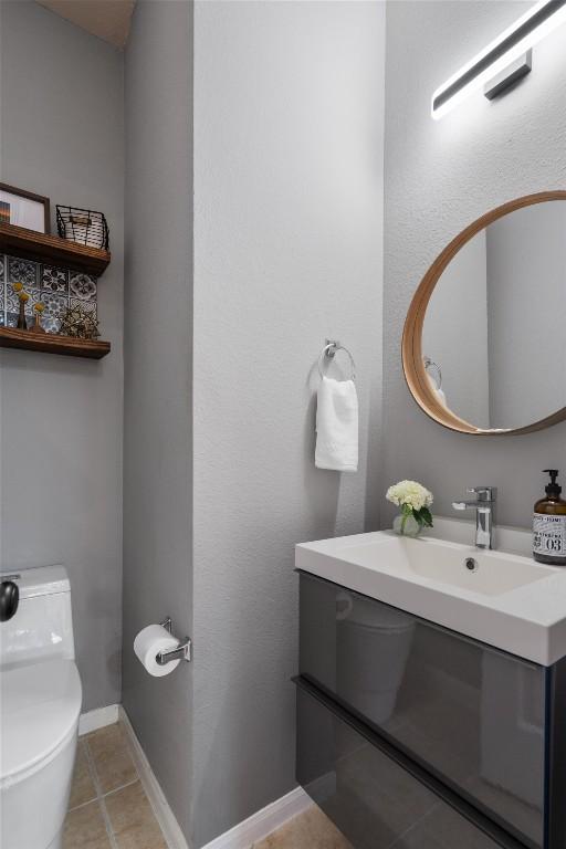 half bath featuring tile patterned flooring, baseboards, a sink, and toilet