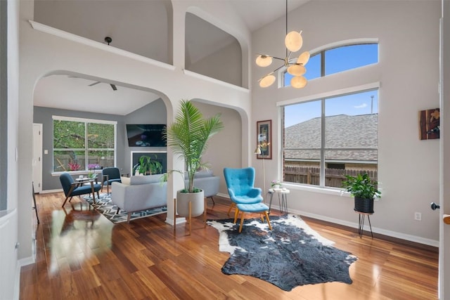 living area with wood finished floors, arched walkways, baseboards, high vaulted ceiling, and a notable chandelier