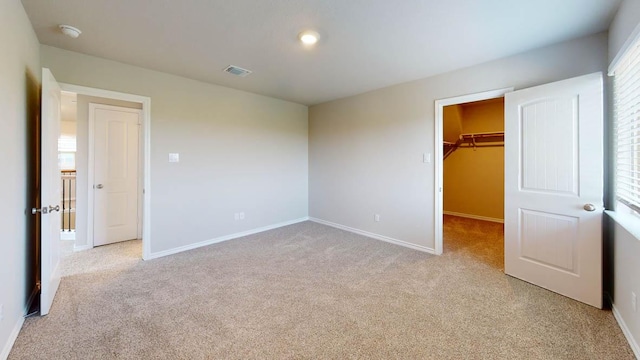 unfurnished bedroom with light carpet, baseboards, visible vents, a spacious closet, and a closet