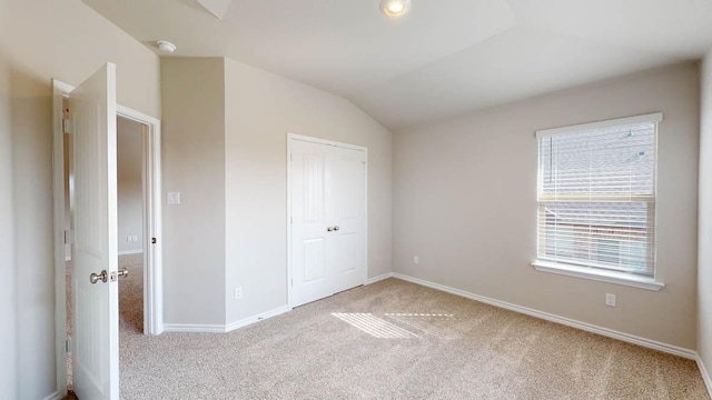 unfurnished bedroom with lofted ceiling, a closet, carpet flooring, and baseboards