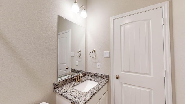 half bath with a textured wall, vanity, and toilet