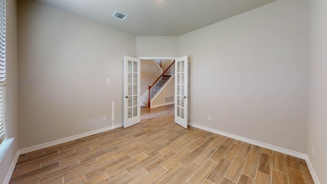 empty room with visible vents, light wood finished floors, baseboards, and french doors
