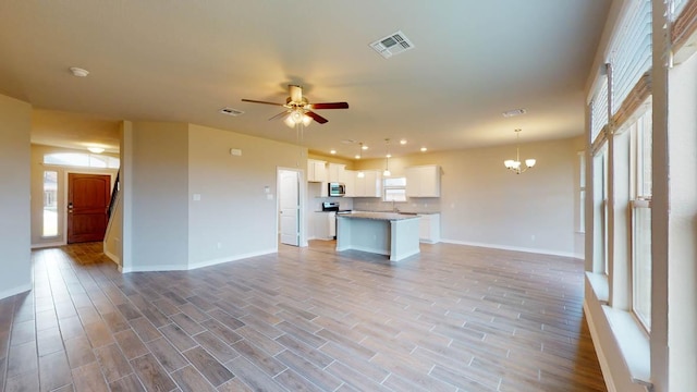 unfurnished living room with ceiling fan with notable chandelier, baseboards, visible vents, and plenty of natural light