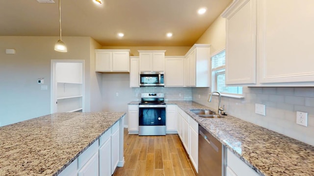 kitchen featuring light stone counters, stainless steel appliances, a sink, tasteful backsplash, and white cabinetry