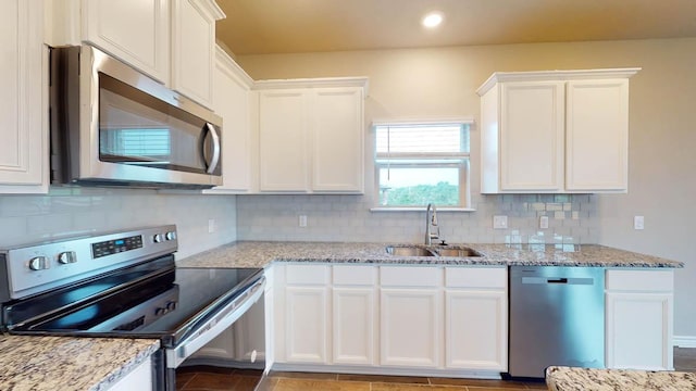 kitchen featuring white cabinets, a sink, light stone countertops, decorative backsplash, and appliances with stainless steel finishes