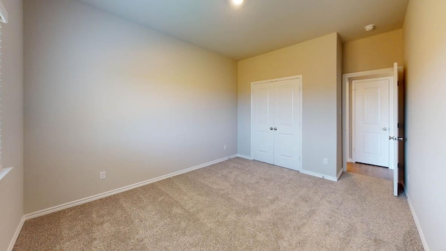 unfurnished bedroom with baseboards, a closet, and light colored carpet