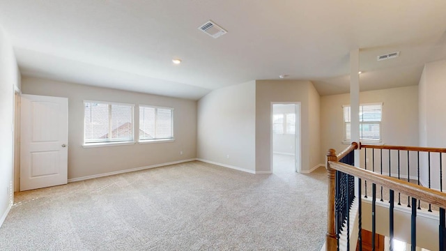 unfurnished room featuring light carpet, vaulted ceiling, visible vents, and baseboards