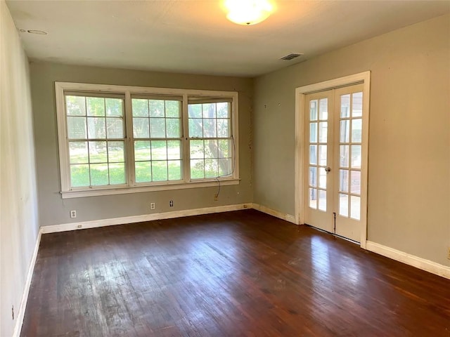 spare room featuring dark wood finished floors, plenty of natural light, visible vents, and baseboards