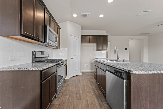 109 Rochester Ln, Hutto, TX 78634 - kitchen featuring appliances with stainless steel finishes, a sink, dark brown cabinetry, dark wood-type flooring, and a center island with sink