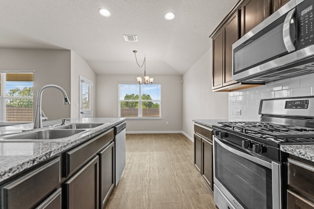 109 Rochester Ln, Hutto, TX 78634 - kitchen featuring appliances with stainless steel finishes, a sink, light wood-type flooring, lofted ceiling, and a chandelier