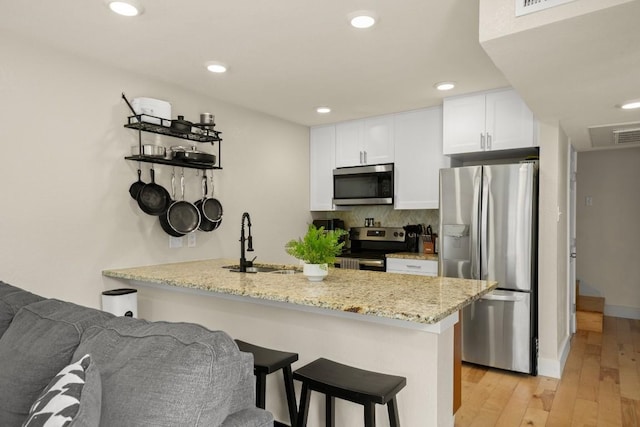 909 Reinli St Unit 104, Austin, TX 78751 - kitchen featuring a kitchen breakfast bar, a sink, light wood-type flooring, white cabinetry, and appliances with stainless steel finishes