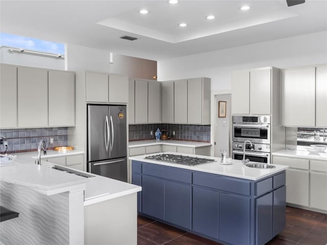 7115 Las Ventanas Dr, Austin, TX 78731 - kitchen featuring appliances with stainless steel finishes, a tray ceiling, recessed lighting, backsplash, and a kitchen island with sink