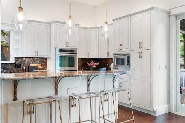 4828 Timberline Dr, Austin, TX 78746 - kitchen with appliances with stainless steel finishes, a breakfast bar area, decorative backsplash, stone countertops, and dark wood finished floors
