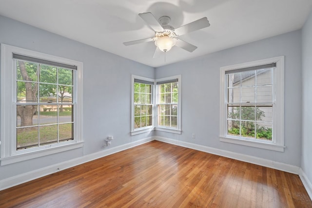 empty room with plenty of natural light, a ceiling fan, baseboards, and wood-type flooring
