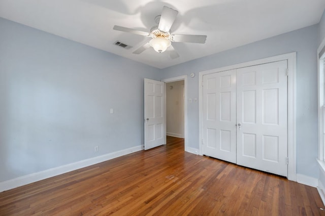 unfurnished bedroom with wood finished floors, visible vents, a closet, baseboards, and ceiling fan