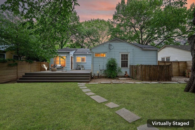 back of house at dusk with a wooden deck, a yard, and a fenced backyard