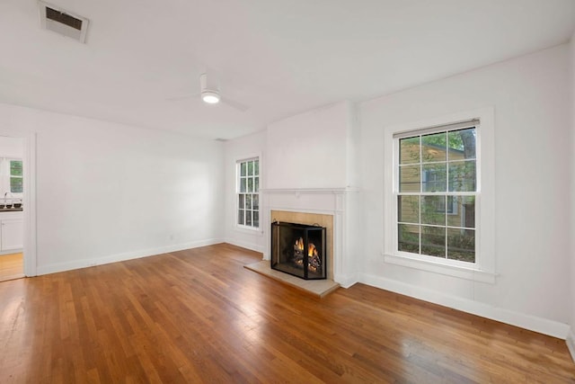 unfurnished living room featuring a wealth of natural light, a lit fireplace, wood finished floors, and visible vents