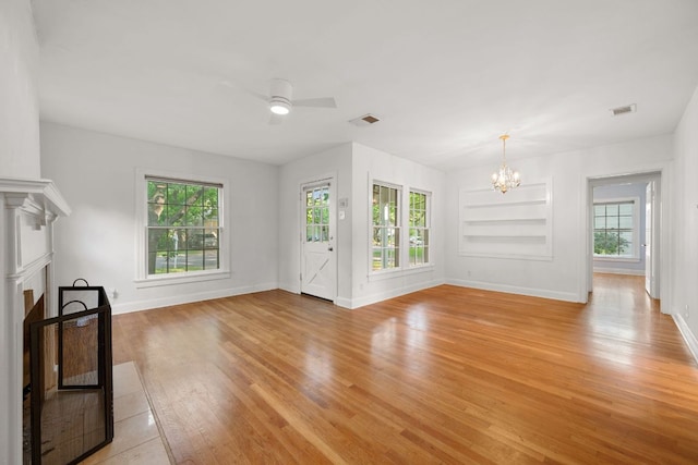 unfurnished living room featuring a wealth of natural light, light wood finished floors, baseboards, and ceiling fan with notable chandelier