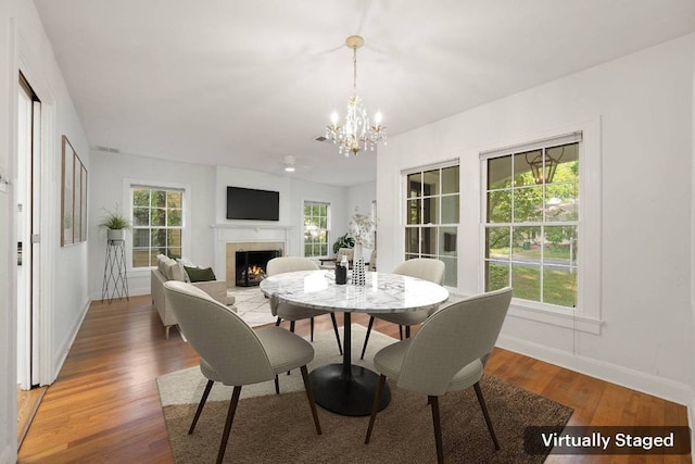 dining space with light wood-style floors, an inviting chandelier, baseboards, and a warm lit fireplace