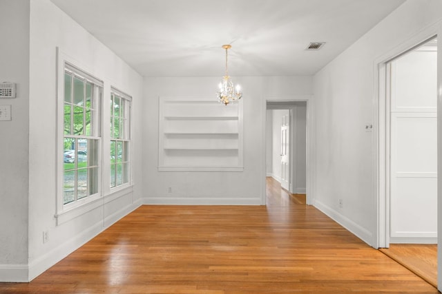 unfurnished dining area featuring baseboards, built in features, light wood-style floors, and a notable chandelier