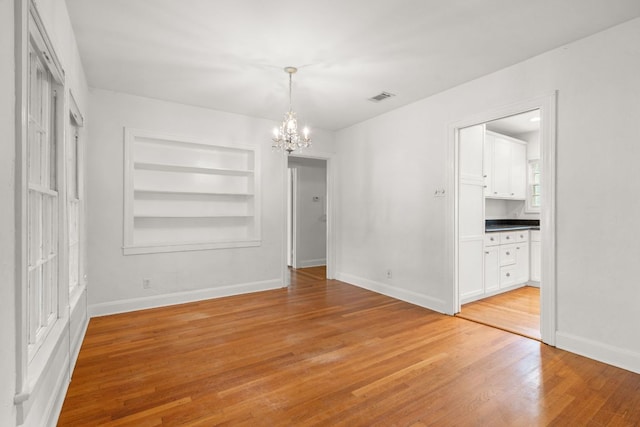 unfurnished dining area with light wood-style flooring, baseboards, visible vents, an inviting chandelier, and built in shelves