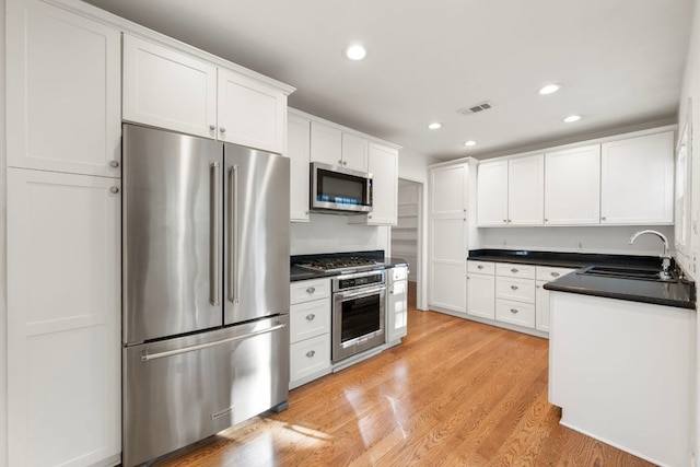 kitchen with light wood finished floors, stainless steel appliances, a sink, visible vents, and white cabinetry