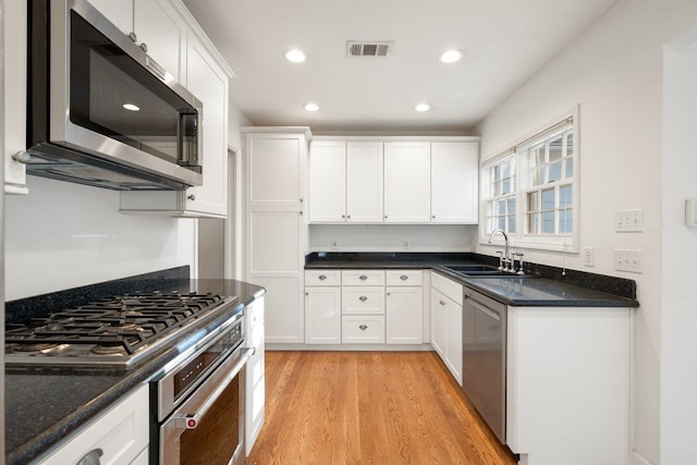 kitchen with a sink, light wood-type flooring, white cabinets, appliances with stainless steel finishes, and recessed lighting