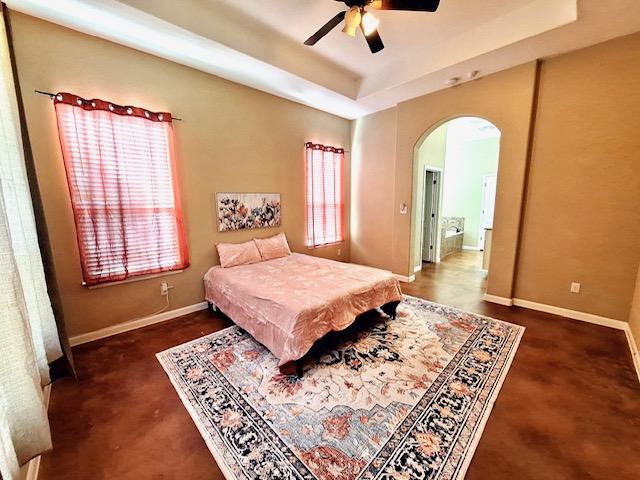 192 W Kaanapali Ln, Bastrop, TX 78602 - bedroom with arched walkways, a tray ceiling, baseboards, ensuite bathroom, and a ceiling fan