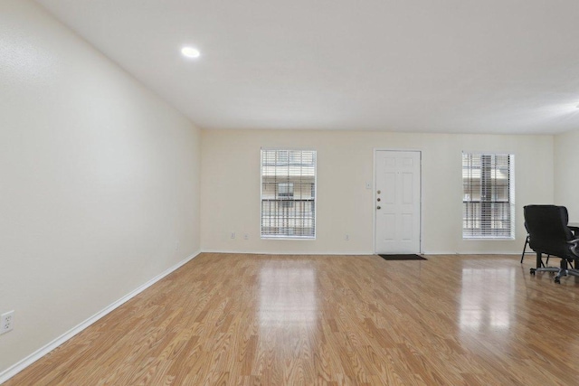 unfurnished living room featuring baseboards, light wood finished floors, and a wealth of natural light