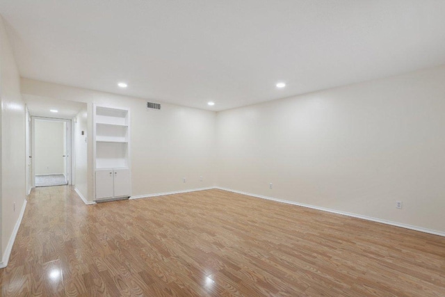empty room featuring baseboards, visible vents, built in shelves, and light wood-style floors