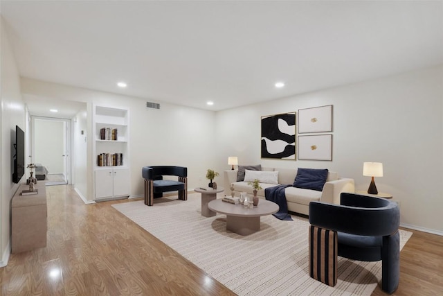living area with visible vents, built in shelves, baseboards, light wood-style floors, and recessed lighting