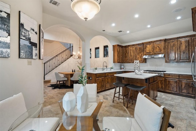 13606 Montview Dr, Austin, TX 78732 - kitchen with under cabinet range hood, light countertops, a kitchen island, a kitchen bar, and light stone finish flooring