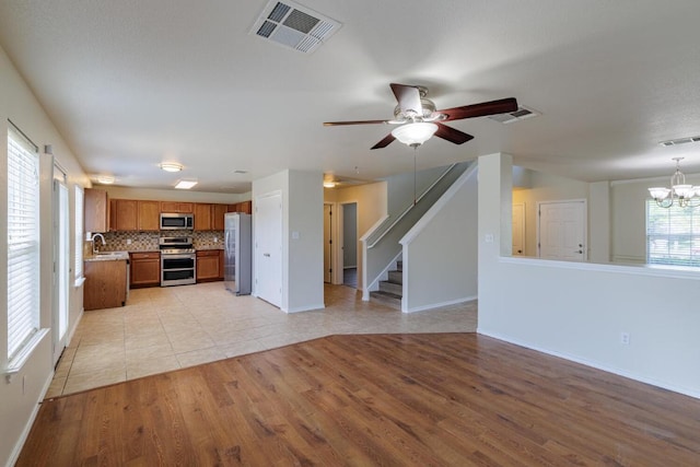 157 Brickyard Ln, Jarrell, TX 76537 - unfurnished living room featuring a chandelier, light wood finished floors, ceiling fan, stairway, and a sink