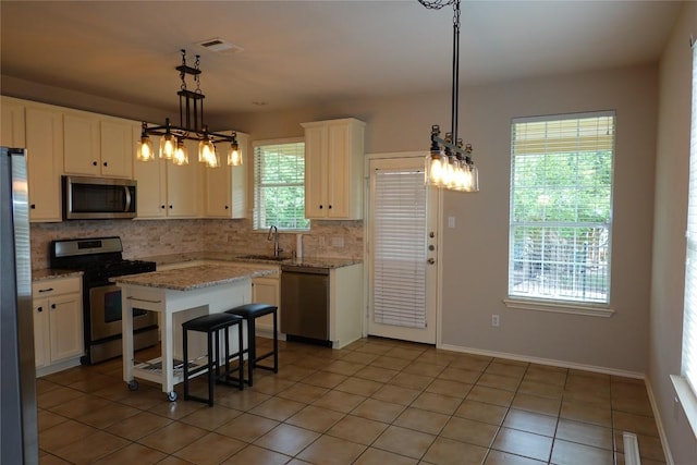kitchen with a sink, light tile patterned flooring, decorative backsplash, appliances with stainless steel finishes, and white cabinetry