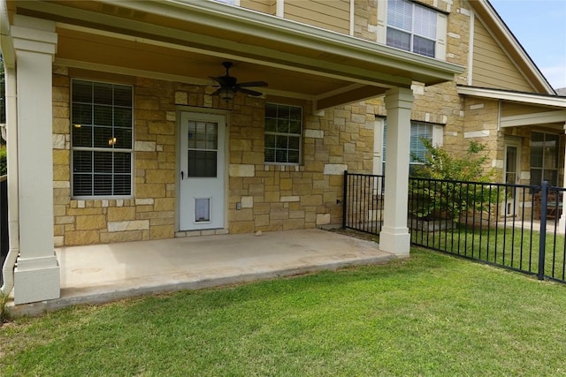 doorway to property with a yard, stone siding, fence, and a ceiling fan
