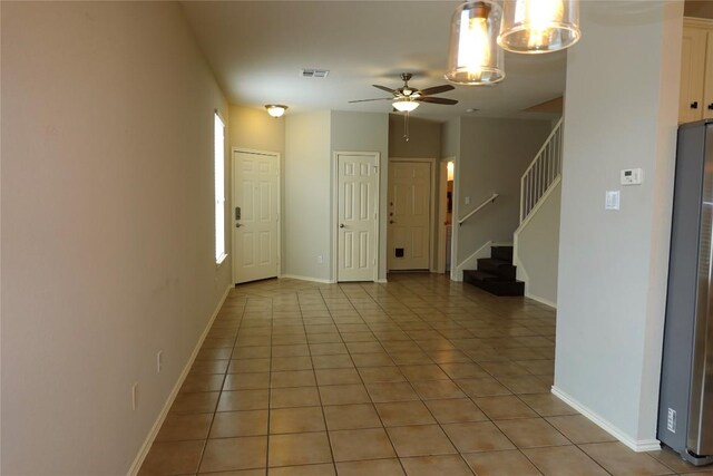 interior space with light tile patterned flooring, baseboards, visible vents, ceiling fan with notable chandelier, and stairs