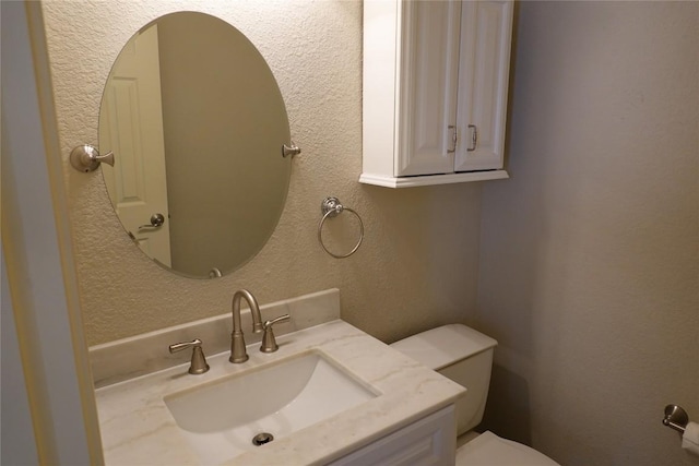 half bath with toilet, a textured wall, and vanity